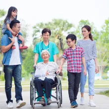 Caregiver pushing wheelchair surrounded by patient's family