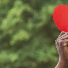 Hands holding red paper heart on green background