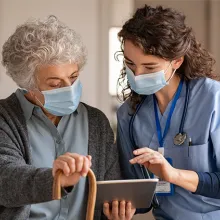 Female nurse reviewing information on tablet with elderly female patient