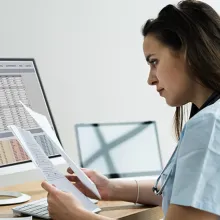 Clinician sitting at a desk reviewing documents in front of a computer