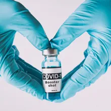 The shape of heart made from hands in gloves holding the covid vaccine booster shot