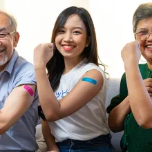 Senior couple and younger woman with bandage on arm show thumb up sign on a couch