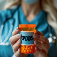 Image of healthcare worker holding a pill bottle that says opioids.