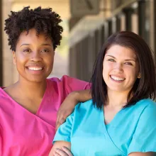 Two nurses leaning on each other and smiling at the camera