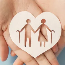 Hands holding a wooden heart with elderly couple icon cutout