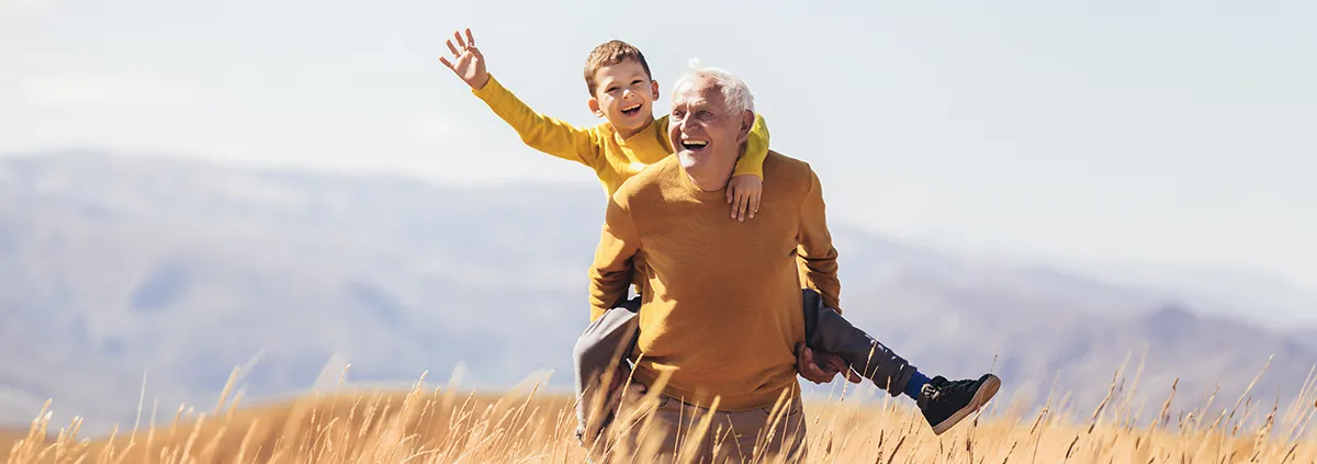 Grandfather carrying his grandson on his back in field