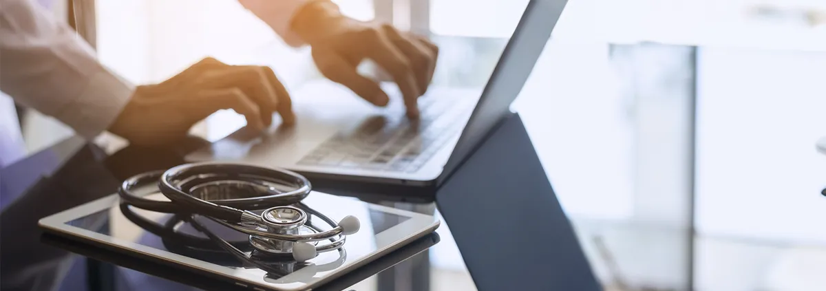 Clinician typing on laptop in a health care setting