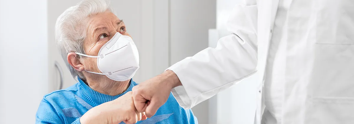 Female Senior adult with ffp2 mask is giving a doctor a fist bump