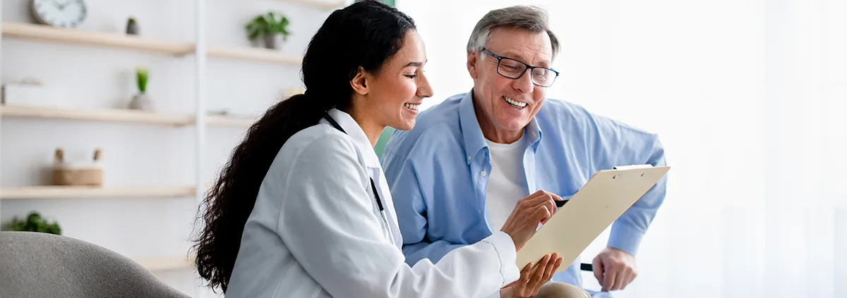 Young clinician asking senior impaired male patient in wheelchair to sign insurance policy at home