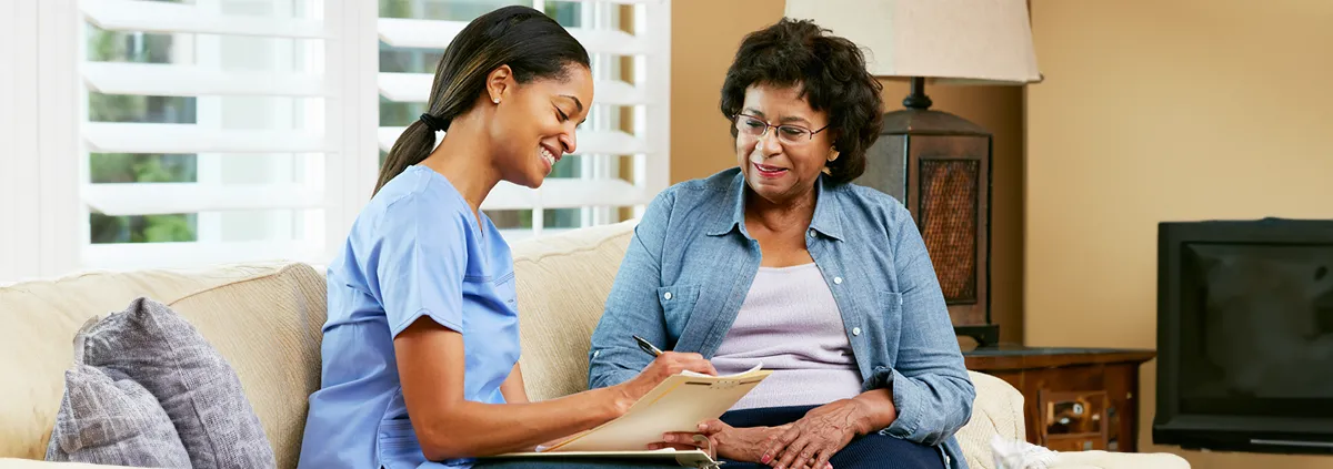 Female healthcare worker filling in a form with a senior woman during a home health visit