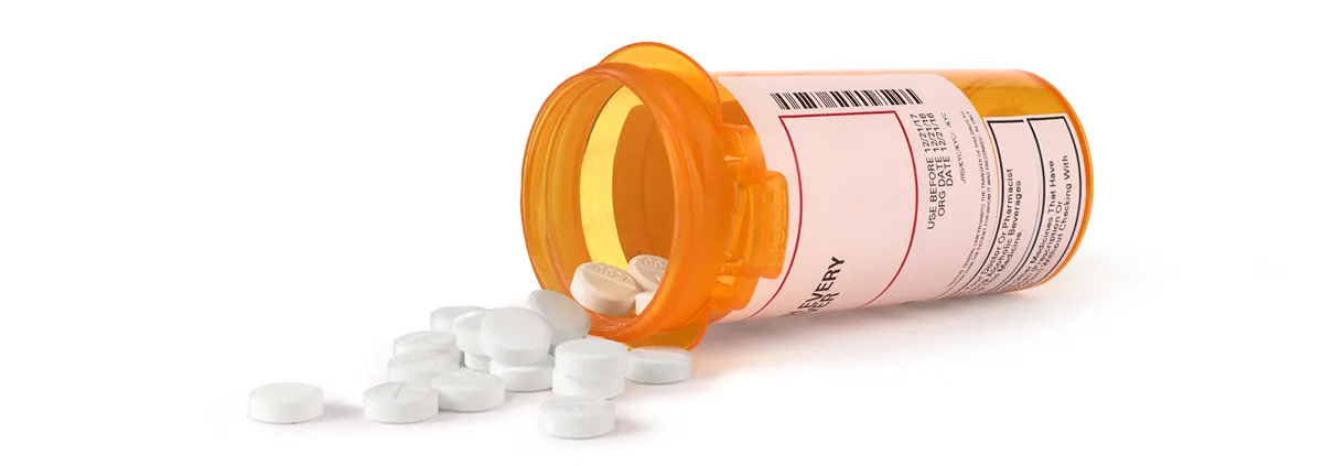 Image of pill bottle on its side with round white pills spilling out