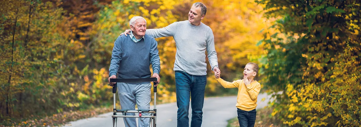 Older male with a walker walking with his son and grandson on a nice autumn day.