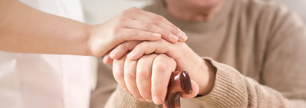 Image of clinician and patient hands. Patient hands are resting on a cane