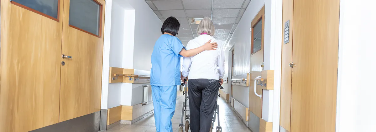 Asian doctor helping elder woman with walker in hospital hallway