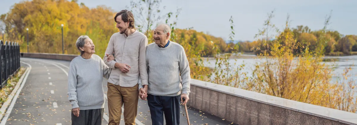 An elderly couple walks in the park with a male assistant or adult grandson. Caring for the elderly, volunteering.