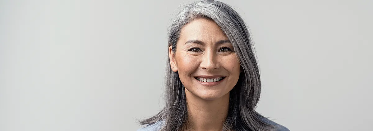 Asian woman with grey hair smiling standing near the wall