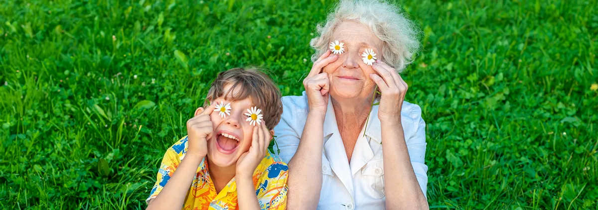 Happy grandmother and grandchild standing on the lawn with chamomiles on their eyes