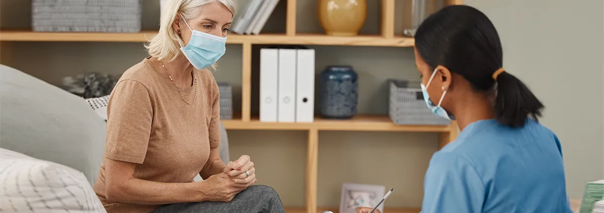 Female nurse speaking with female patient with mask on