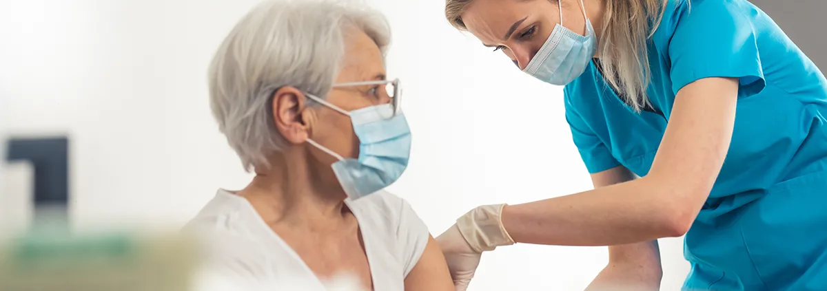 Female nurse with mask and blue nurse outfit giving female elderly patient with mask the vaccination shot