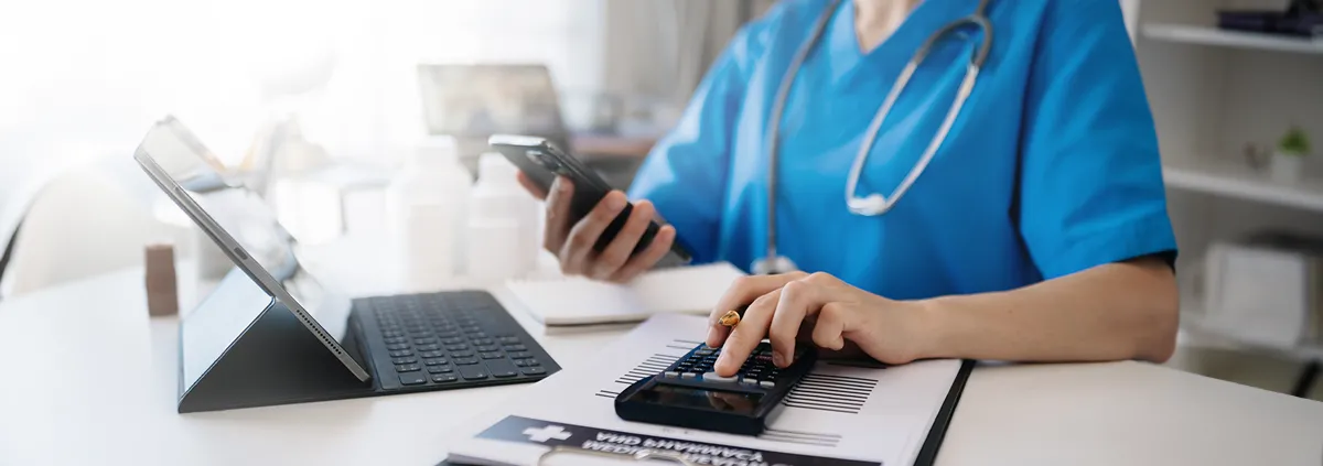 Healthcare professional using laptop and calculator at desk