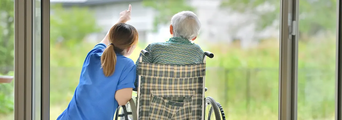 Clinician sitting with a senior male patient in a wheelchair their backs facing the views and they looking out of a window