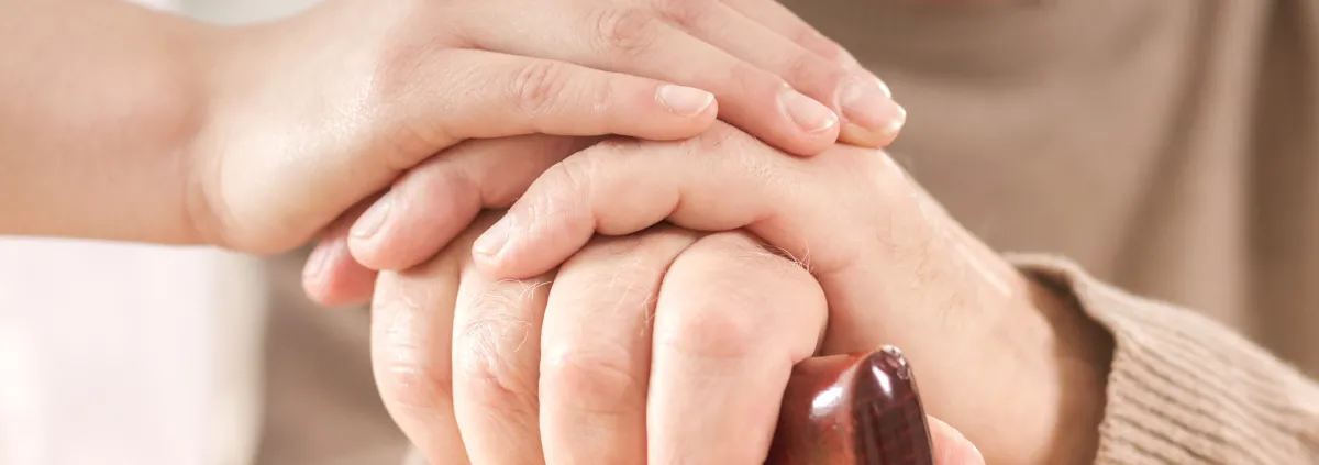 Image of healthcare provider putting their hands on top of an older adult (with a cane) hands. 