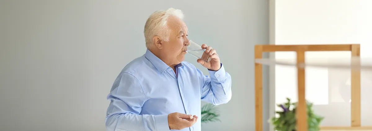 Elderly man drinking water with medication in his hand