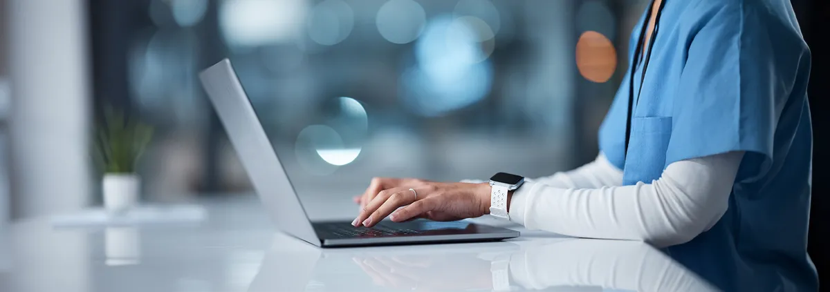 Healthcare staff typing on a laptop in a healthcare setting.