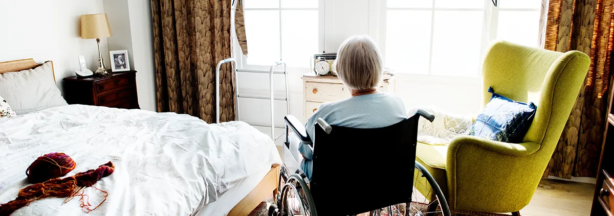 elderly person sitting in wheelchair looking out a window in a home setting