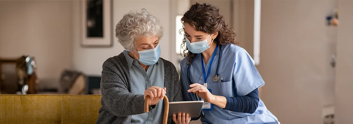 Female nurse reviewing information on tablet with elderly female patient