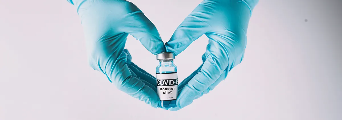 Gloved clinician making a heart with hands holding a vaccine vile 