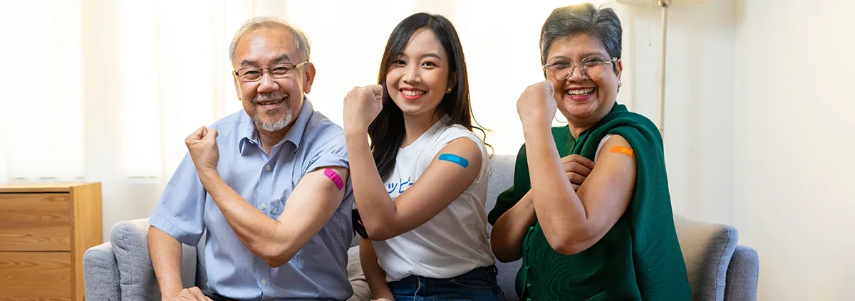 Senior couple and younger woman with bandage on arm show thumb up sign on a couch