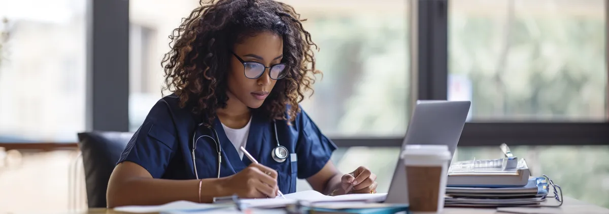 Clinician reading on laptop while taking notes