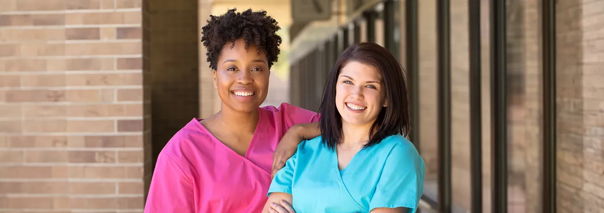 Two nurses leaning on each other and smiling at the camera