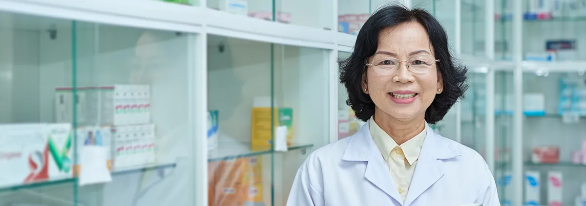 A pharmacist standing in the pharmacy smiling at the camera