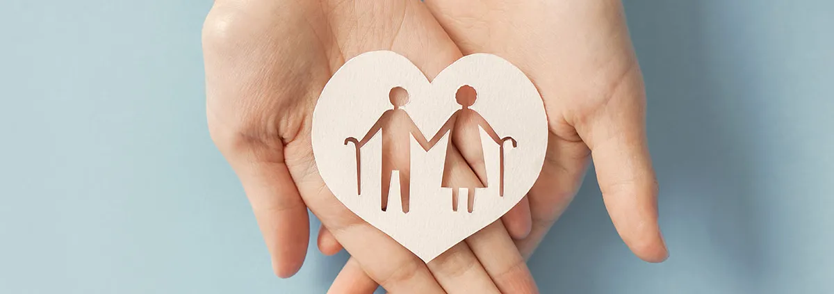 Hands holding a wooden heart with elderly couple icon cutout