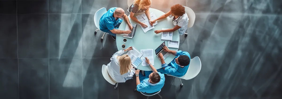 Group of providers sitting around a circle table with laptops, documents, etc. 