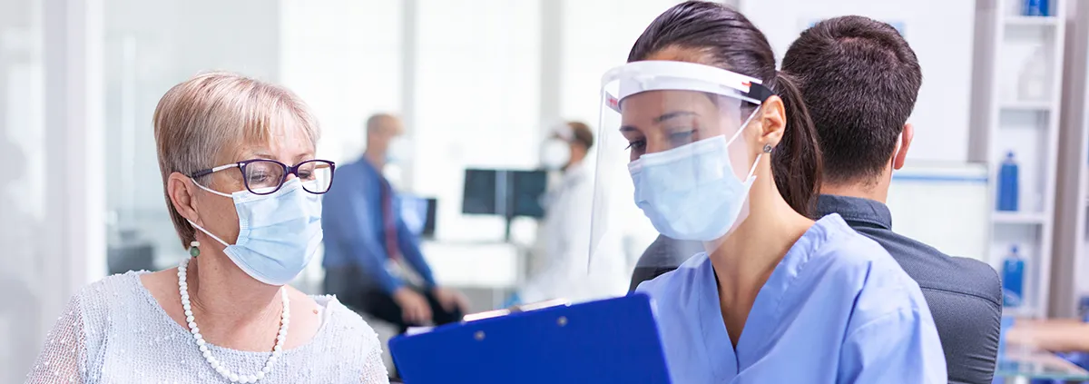 Disabled senior woman having a discussion with clinician in hospital hallway wearing face mask