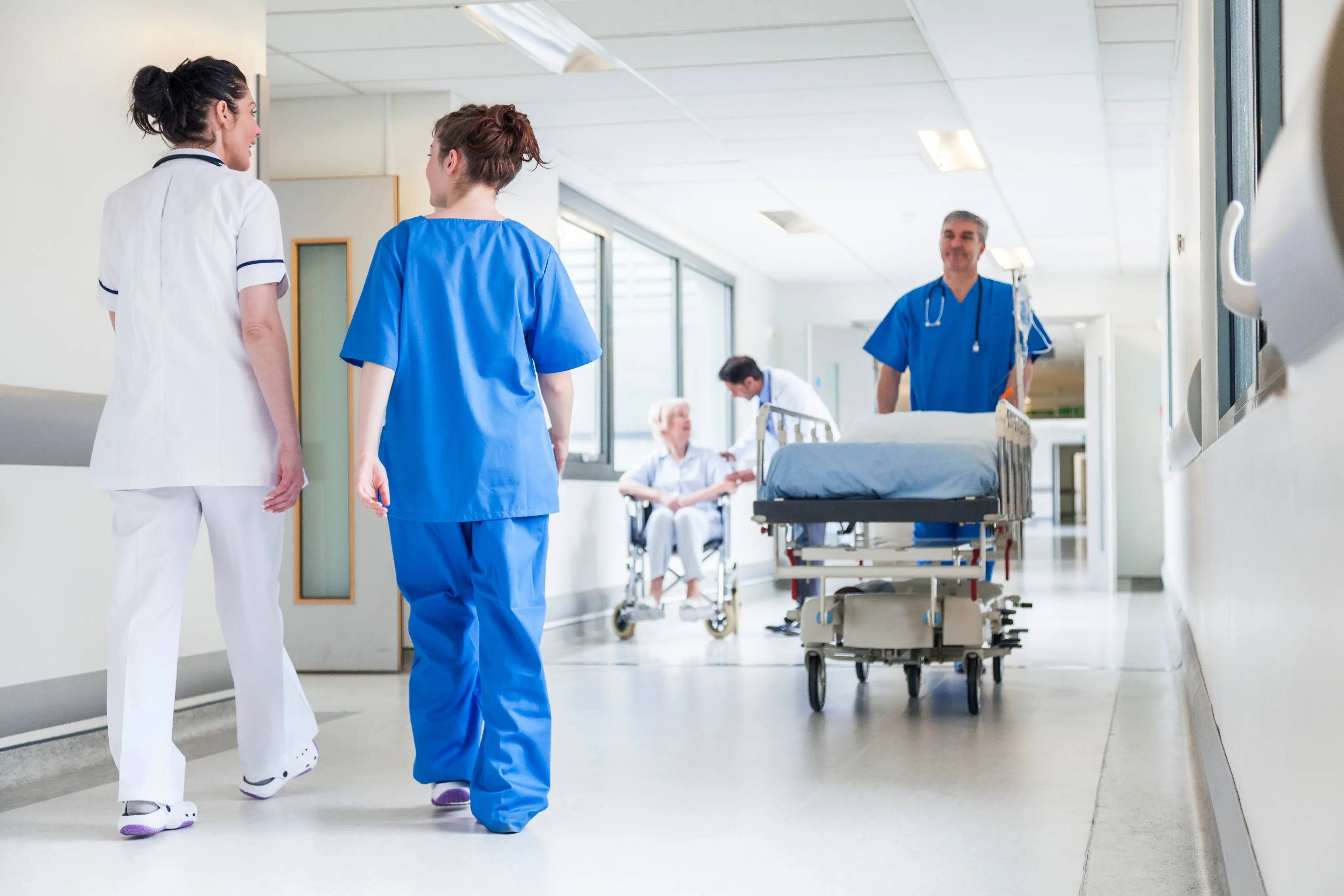 Male nurse pushing stretcher gurney bed in hospital corridor with doctors & senior female patient